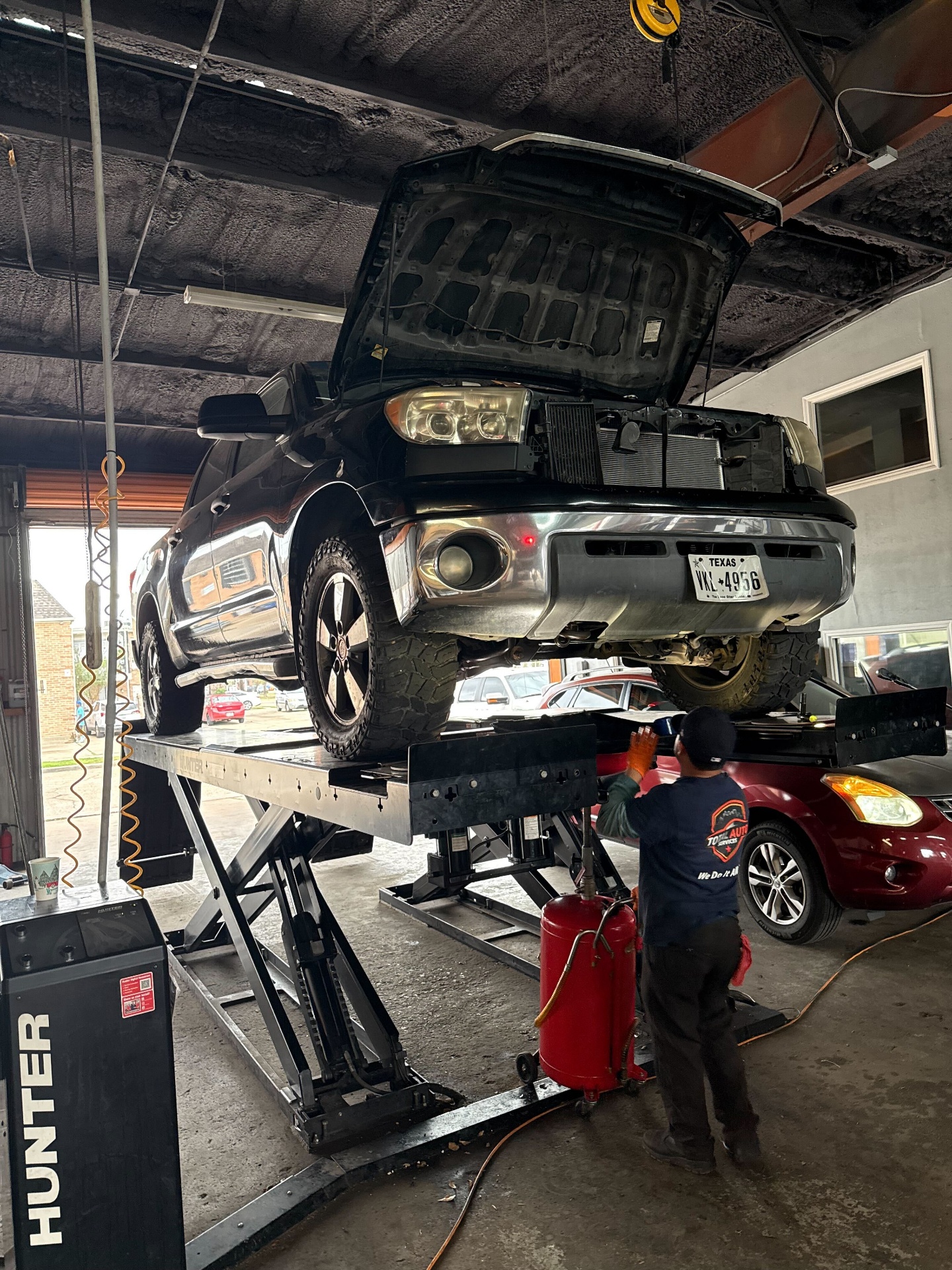 Technician performing suspension work on a lifted Toyota Tundra at Total Auto Services